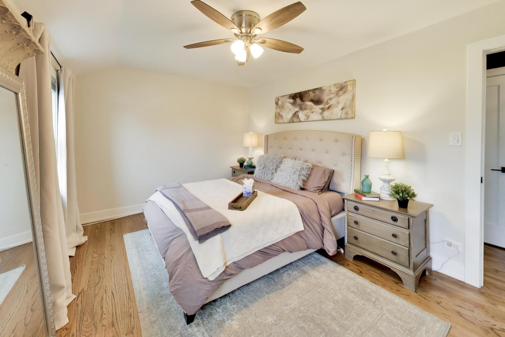 Staged bedroom with a tufted bed, mauve bedding, hardwood floors, and a wood dresser.