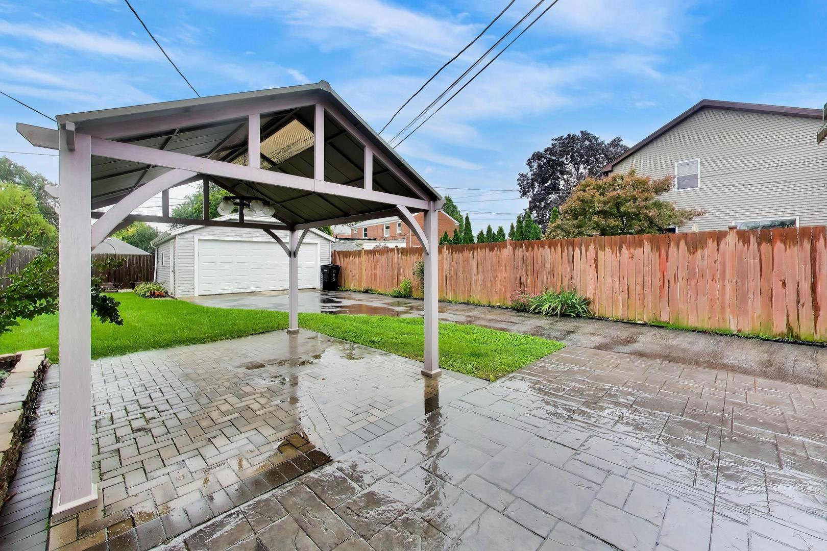 Backyard patio beneath a covered pavilion, with a detached garage and wooden privacy fence.