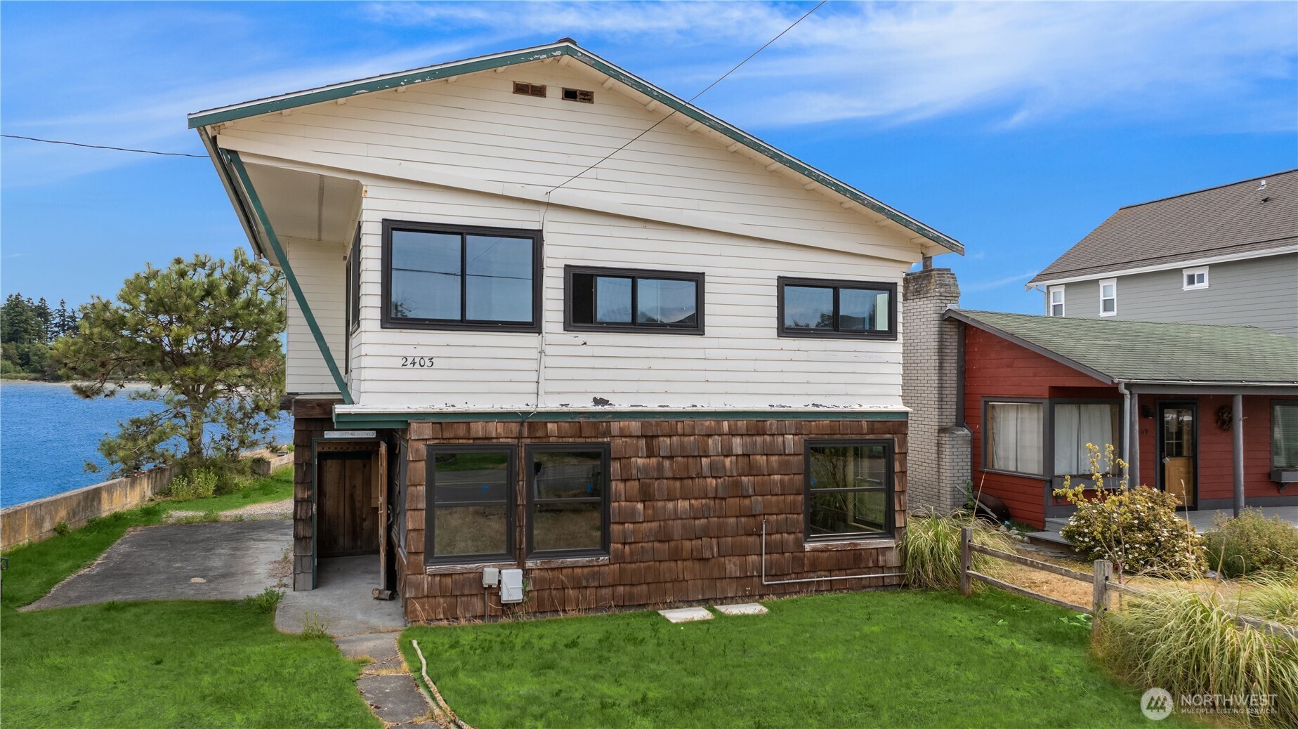 Waterfront home's white-and-brown exterior beside the water, with a green lawn and neighboring red house.