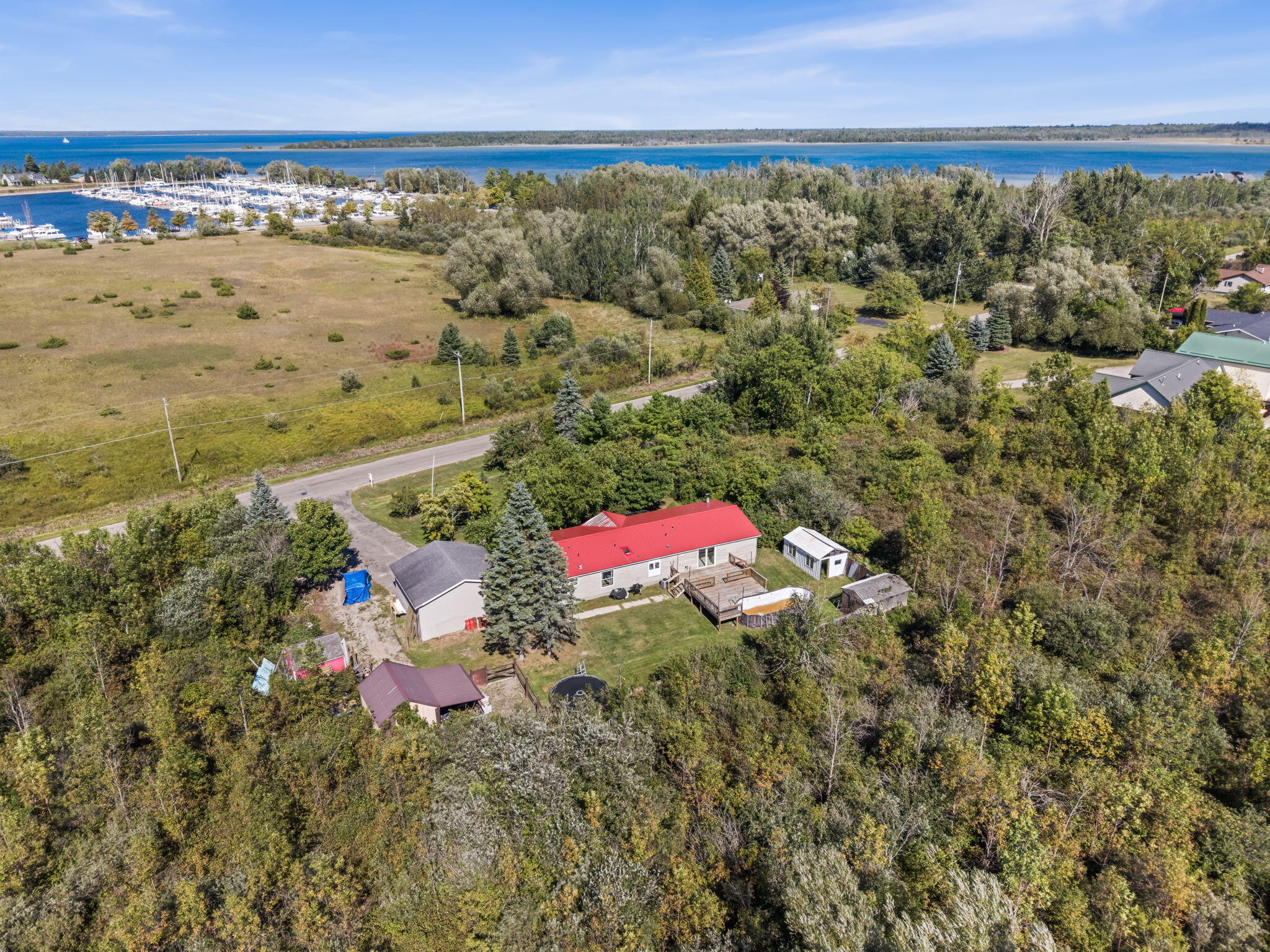 Aerial view of a red-roofed home amid trees, with a marina and blue water beyond.