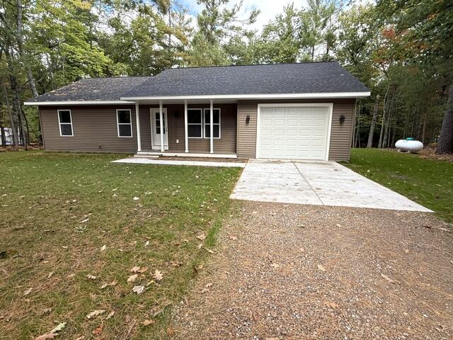 Single-story brown home with a white garage door, concrete driveway, and wooded surroundings.