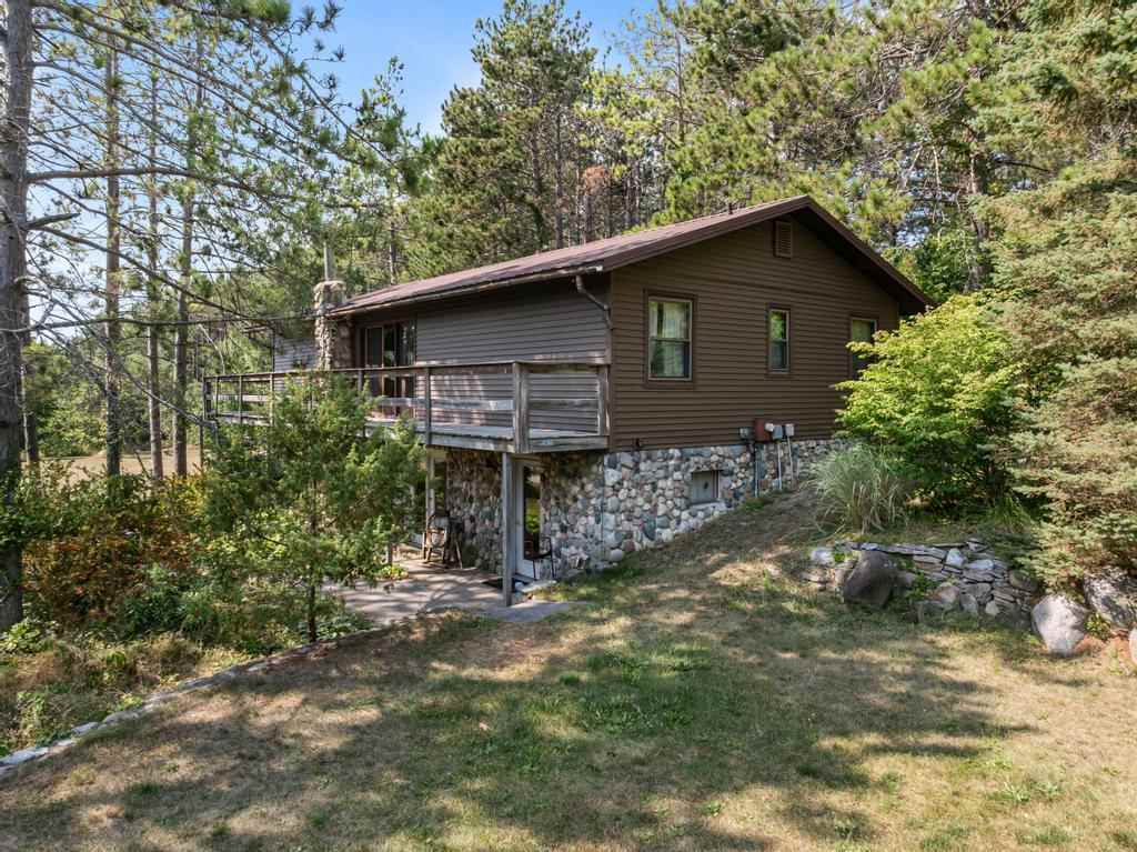 Brown-sided house with a stone foundation and raised deck among trees.