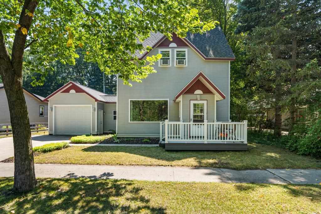 Two-story gray house with attached garage and white-railed porch beneath leafy trees.