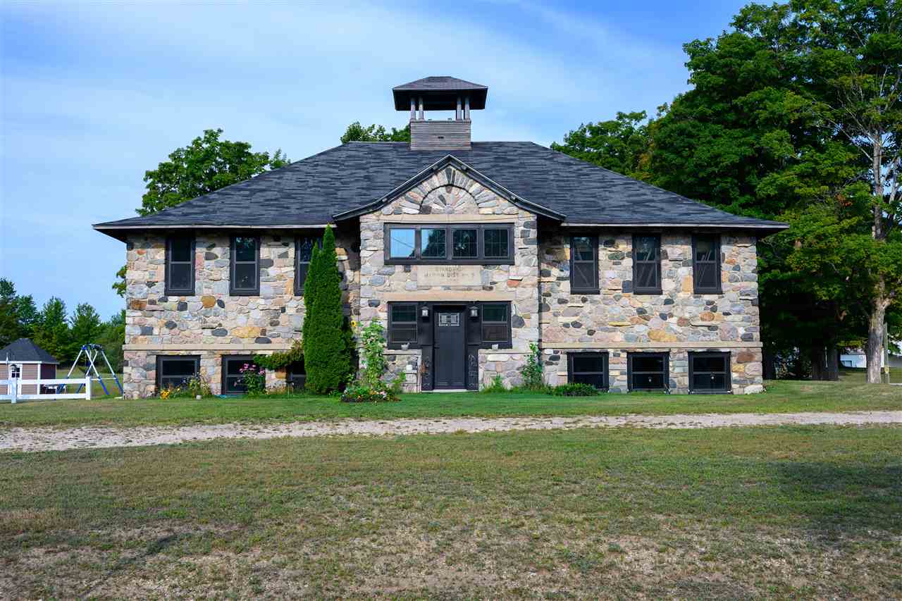 Two-story stone building with a central cupola and broad dark roof, set on a grassy lot.
