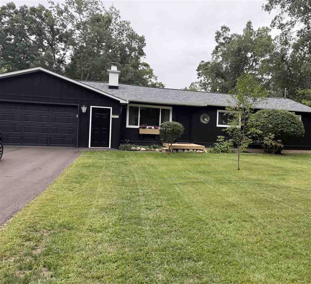 Dark single-story home with a two-car garage, flower box, and broad green lawn.
