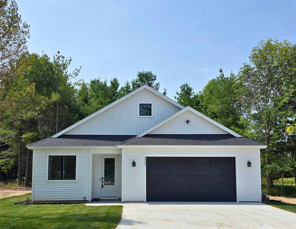 White single-story house with a double garage, concrete driveway, and trees around the yard.
