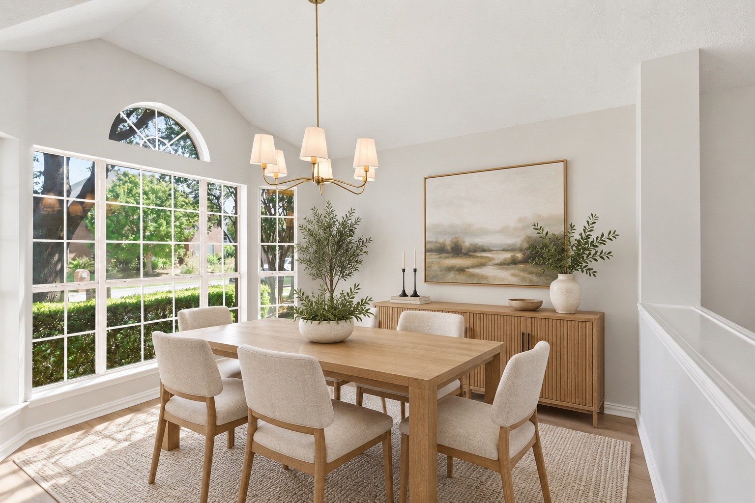 Dining room with a wood table, upholstered chairs, and large windows overlooking leafy landscaping.