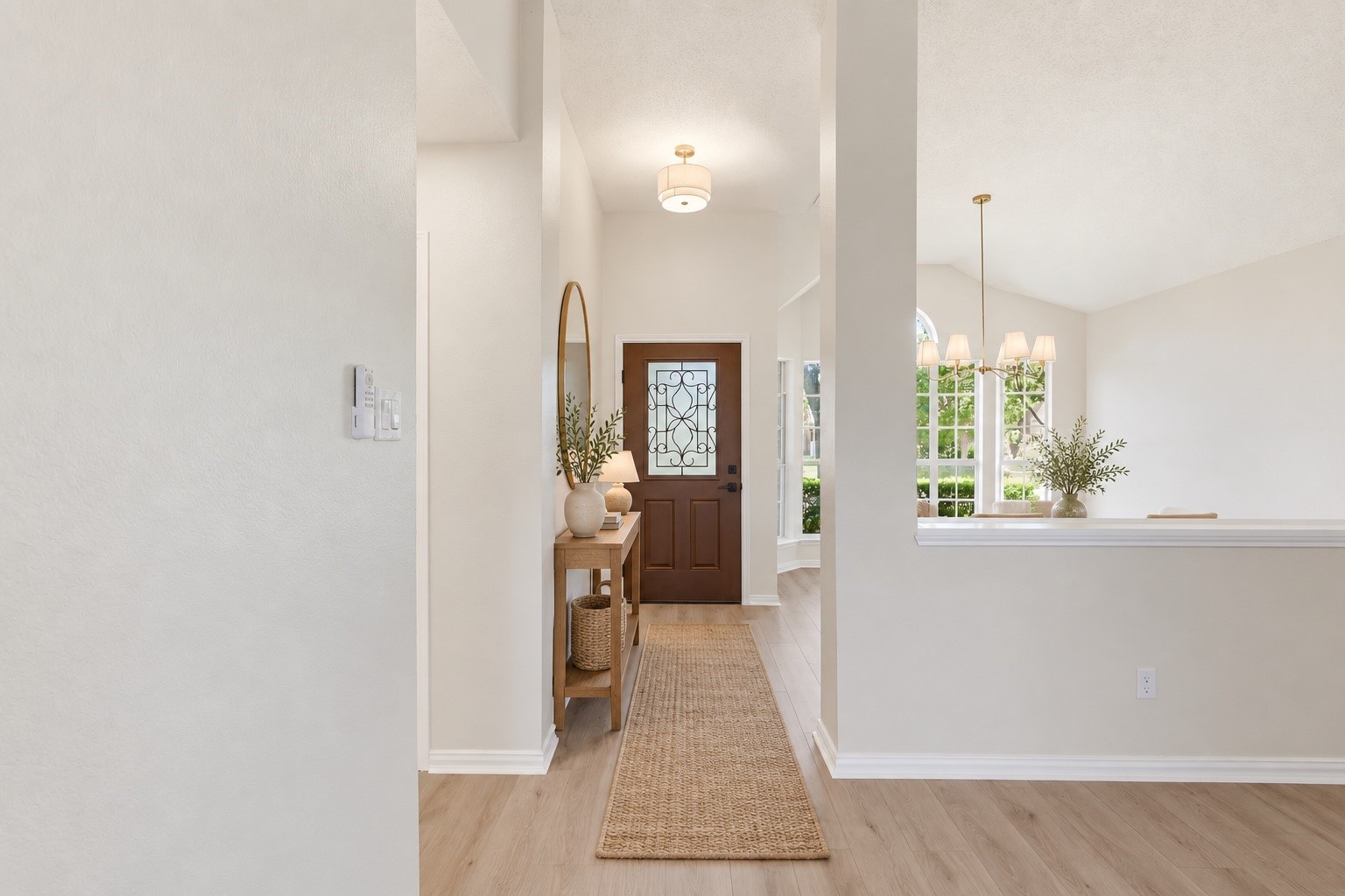 Bright entryway with a decorative glass front door, console table, oval mirror, and woven runner.