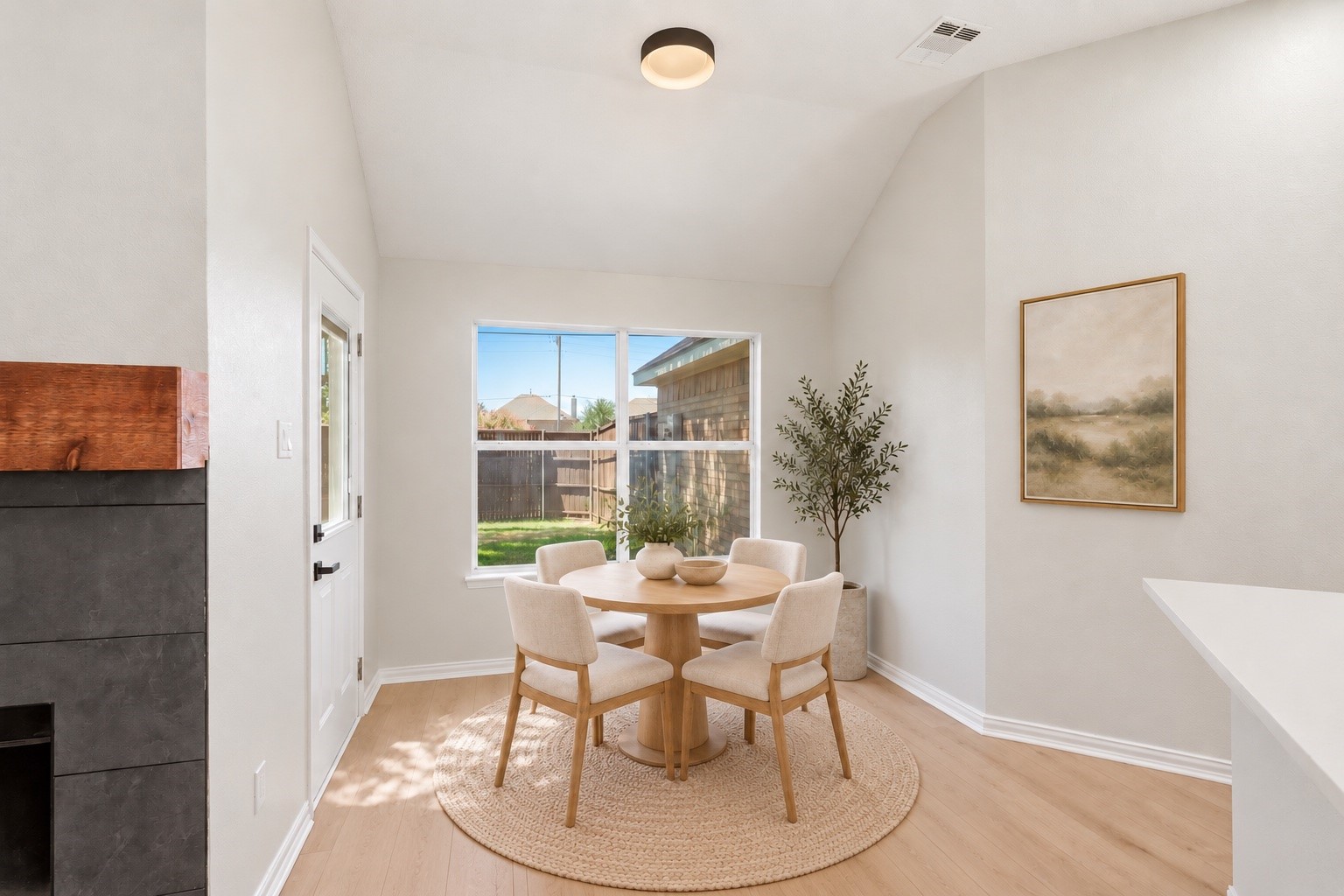 Dining nook with a round wooden table, four chairs, and large windows overlooking a fenced backyard.
