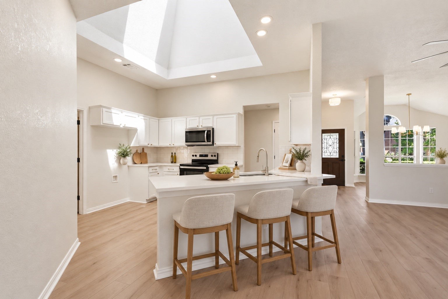 Open-plan kitchen with white cabinets, a large island and three stools beneath a vaulted skylight.
