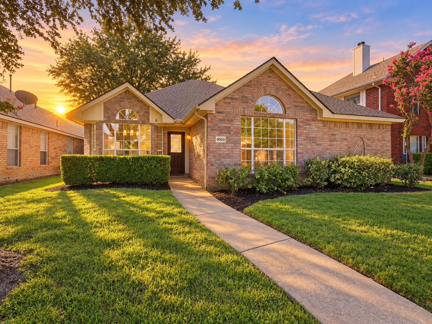 Brick house with arched windows, a landscaped front yard, and a walkway at sunset.