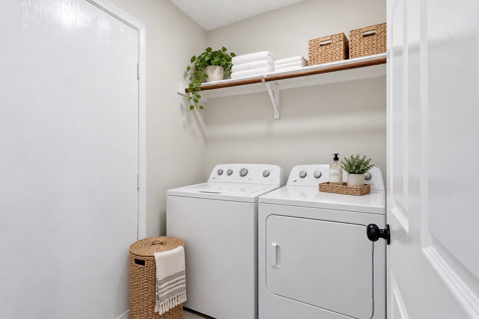 Laundry room with white washer and dryer, woven baskets, folded towels, and a trailing plant.