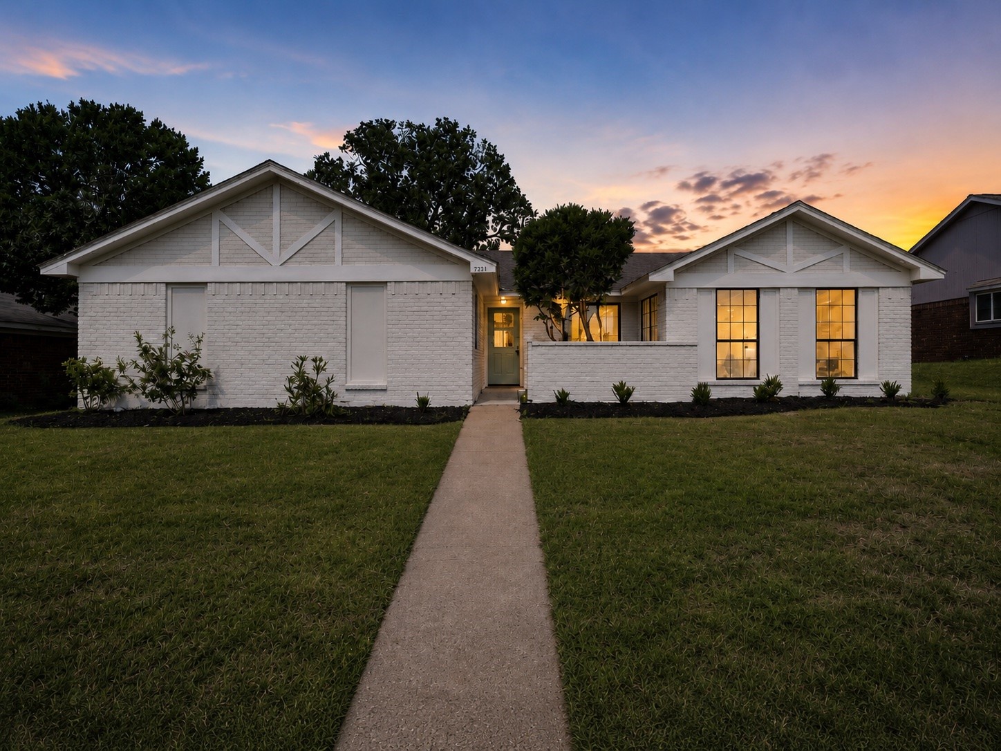 White brick single-story home with a central walkway and warmly lit windows at dusk.