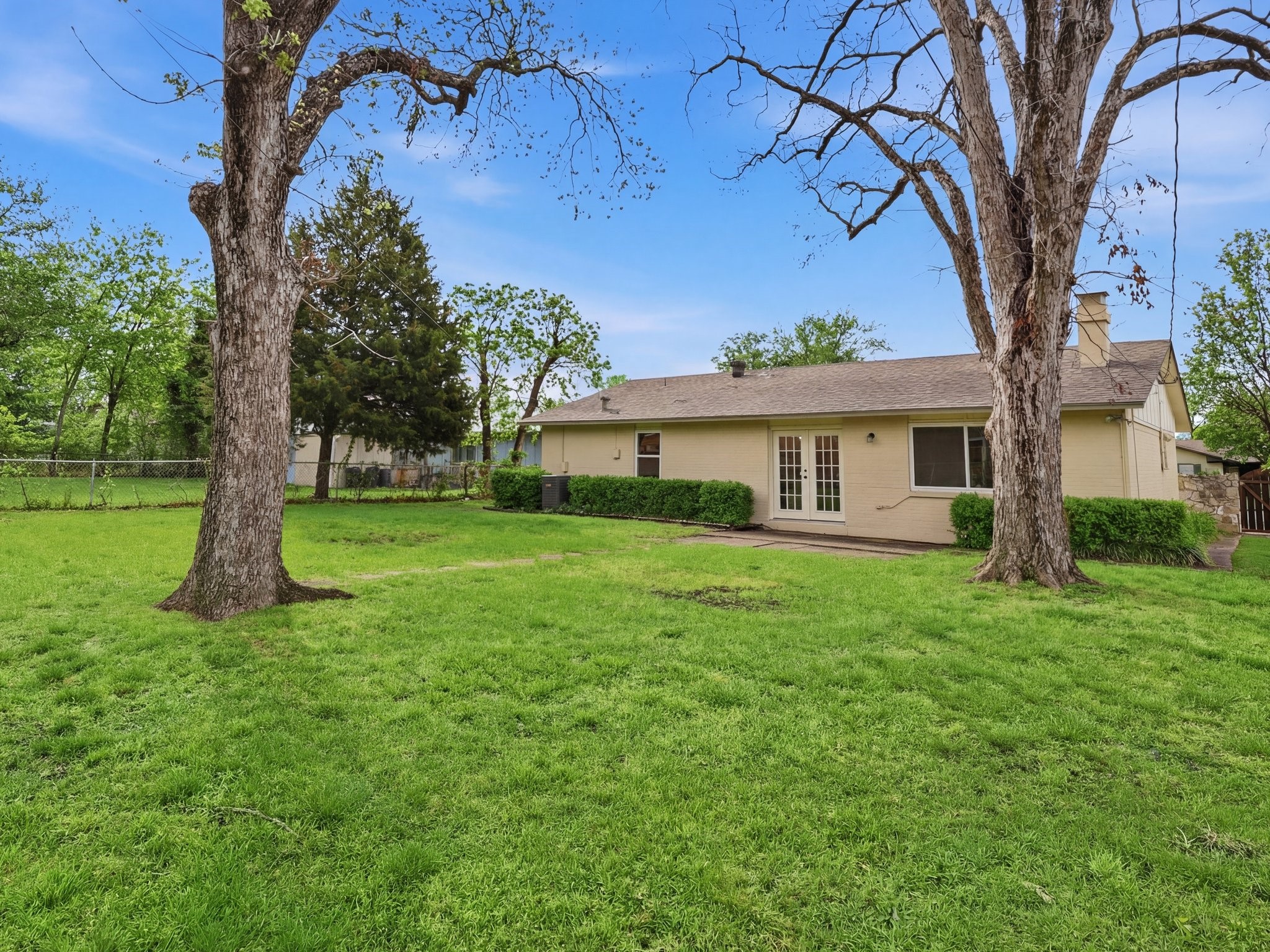 Single-story beige house behind a broad lawn, framed by two mature trees.
