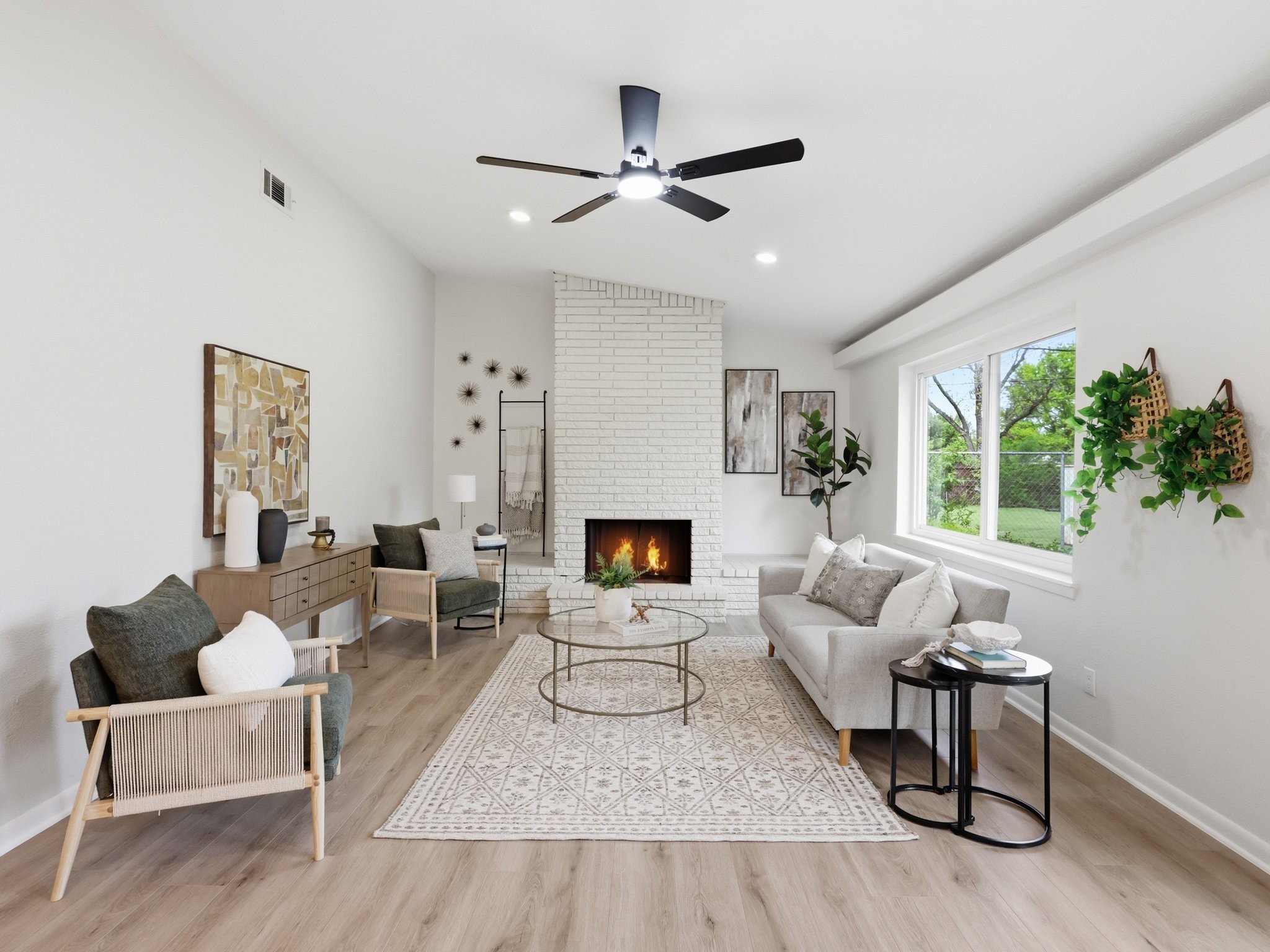 Staged living room with a white brick fireplace, large windows, and seating around a glass coffee table.