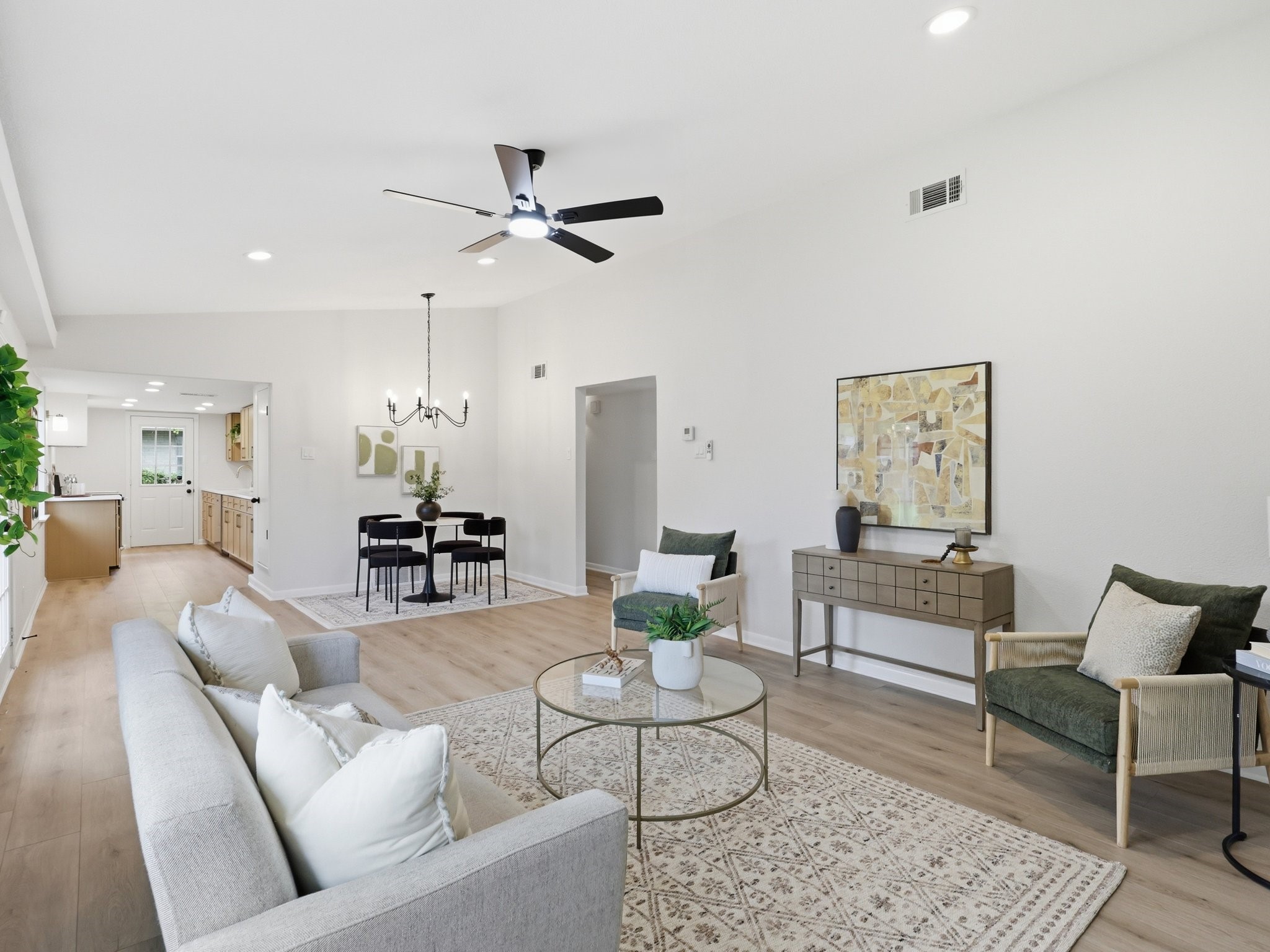 Open-plan living room with light wood floors, green accent chairs, and dining area beyond