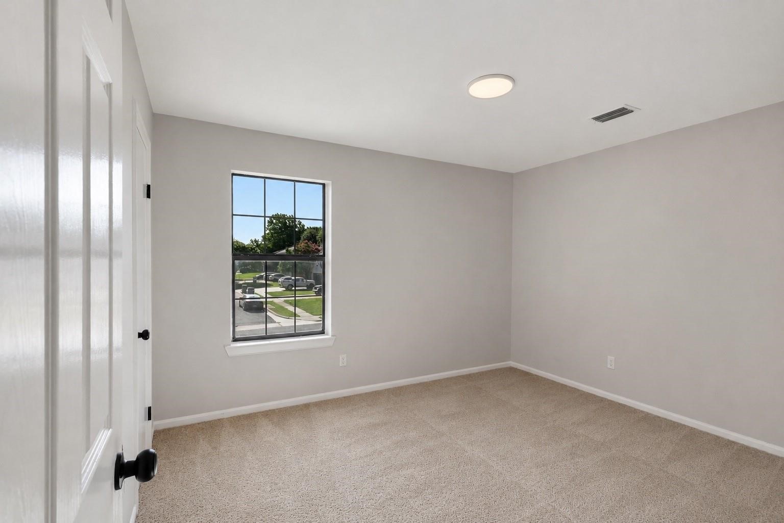 Empty bedroom with beige carpet and a black-trimmed window.