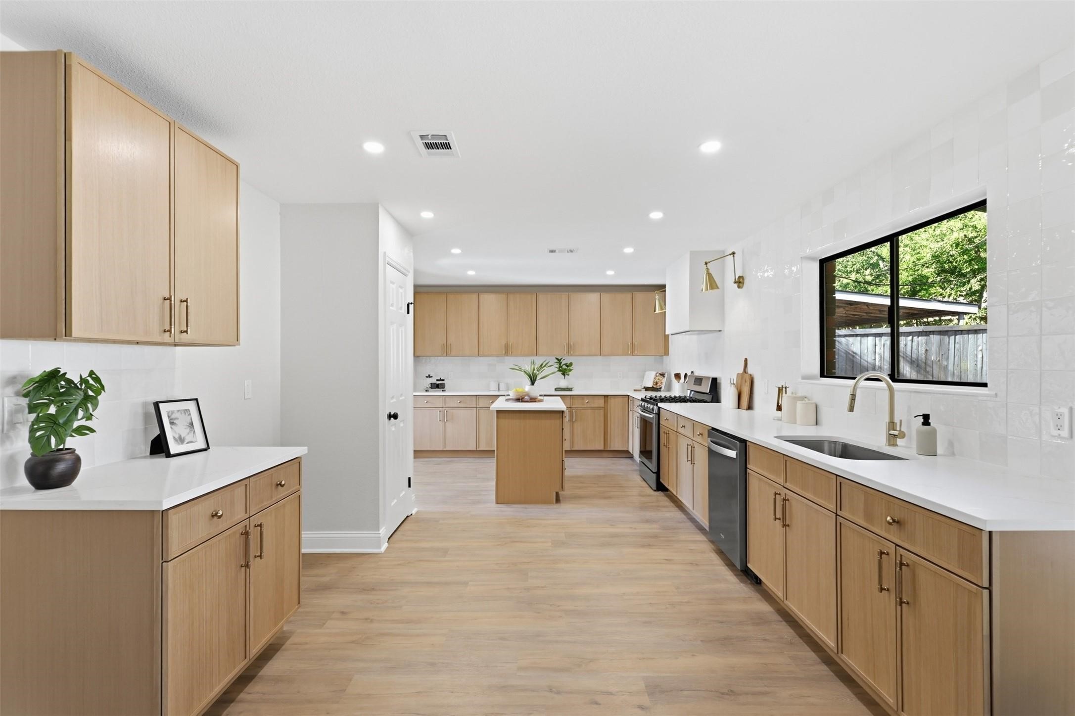 Renovated kitchen with light wood cabinets, a central island, and a large window overlooking a fenced yard.