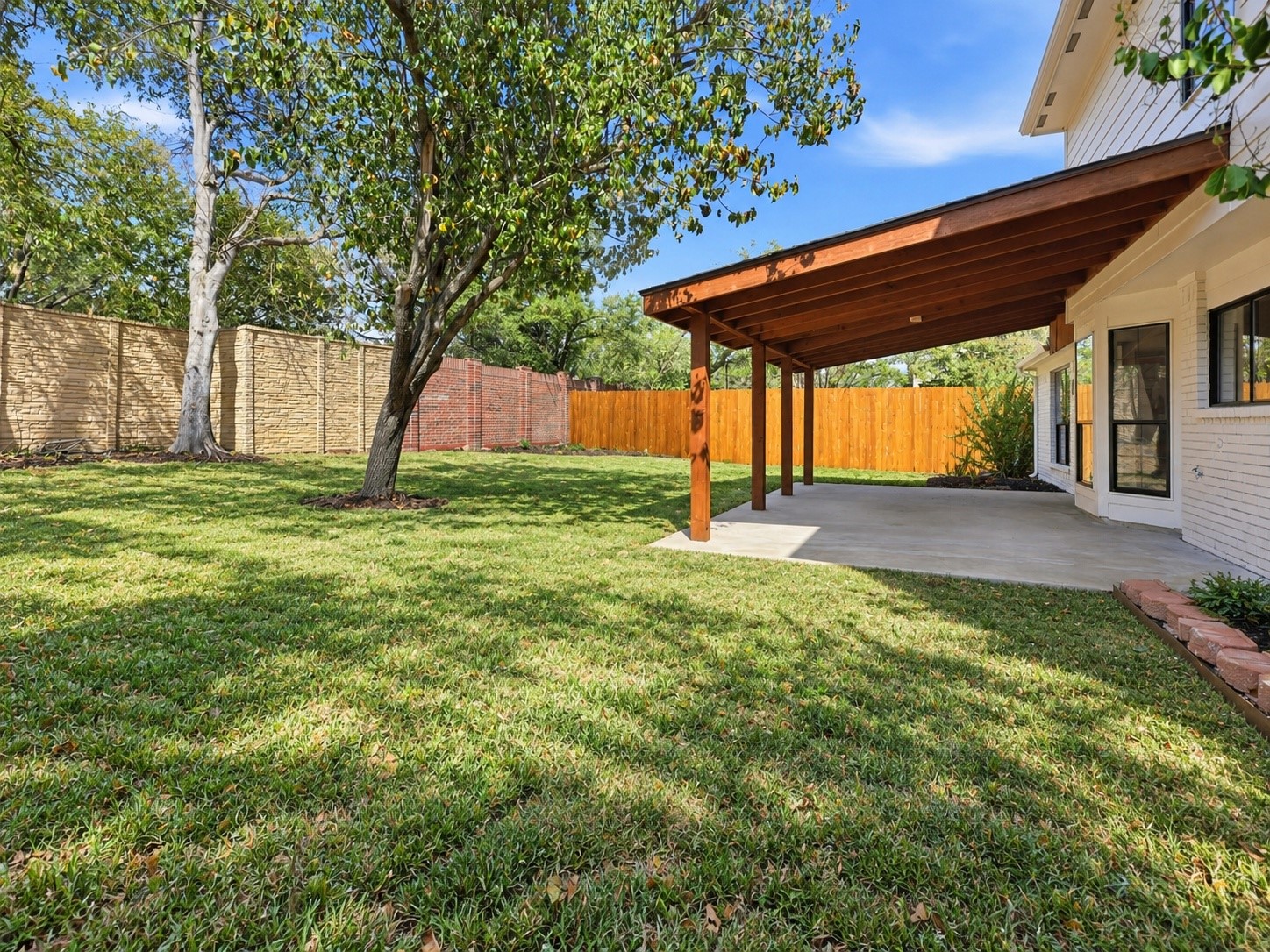 Backyard with a covered timber patio, broad lawn, mature trees, and fenced perimeter.