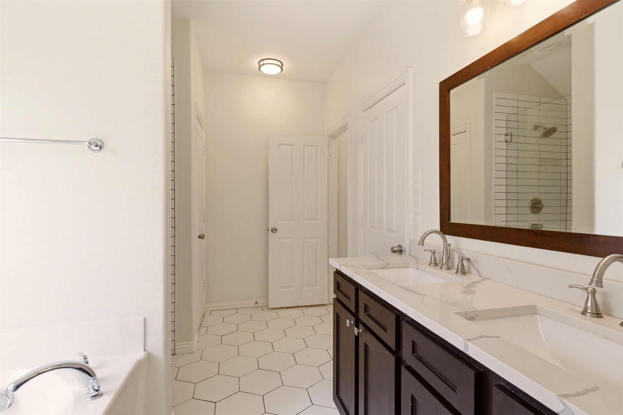 Bathroom with a dark wood double vanity, large framed mirror, hexagonal tile floor, and bathtub.