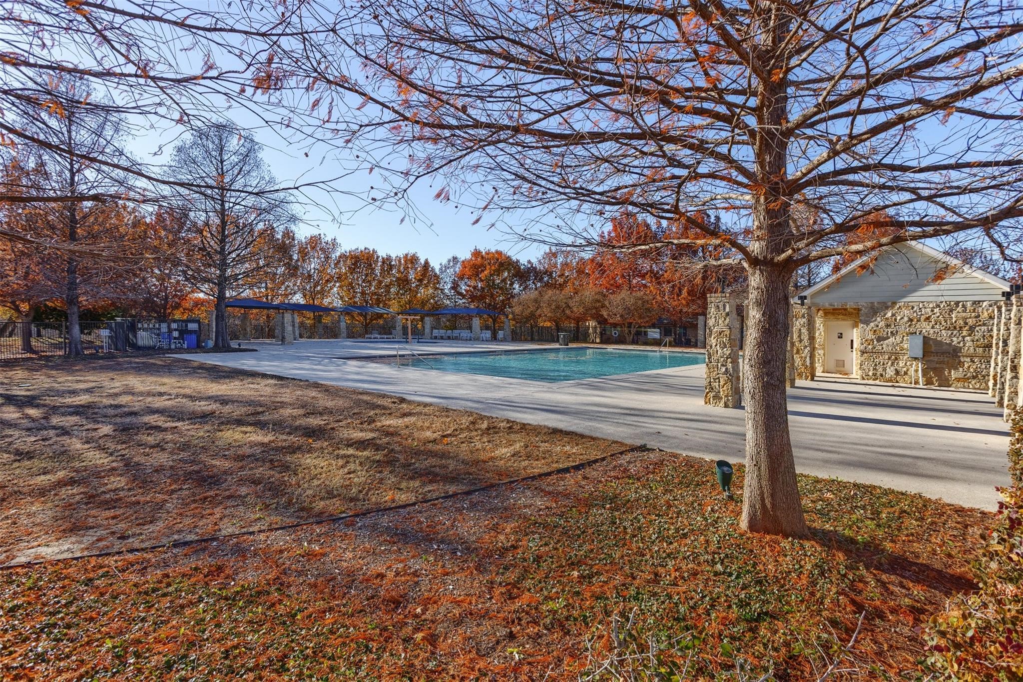Community swimming pool beside a stone building, framed by autumn trees.