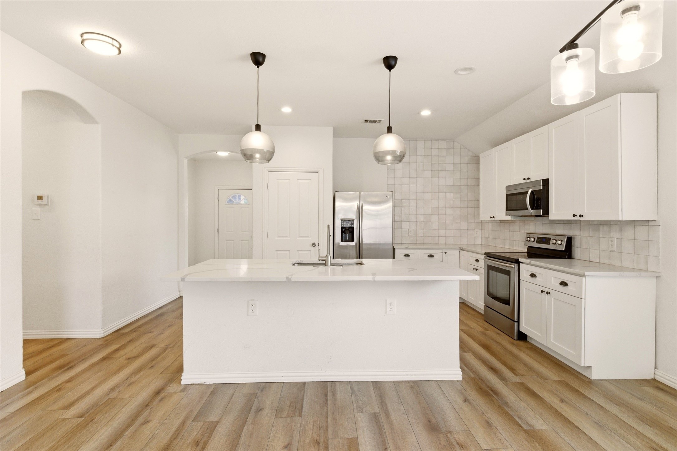 Kitchen with a large white island, stainless steel appliances, and wood-look floors.