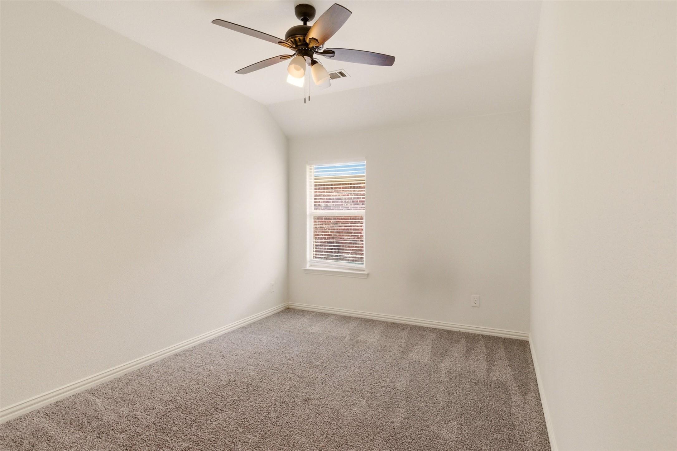 Empty carpeted bedroom with a ceiling fan and a window with blinds.