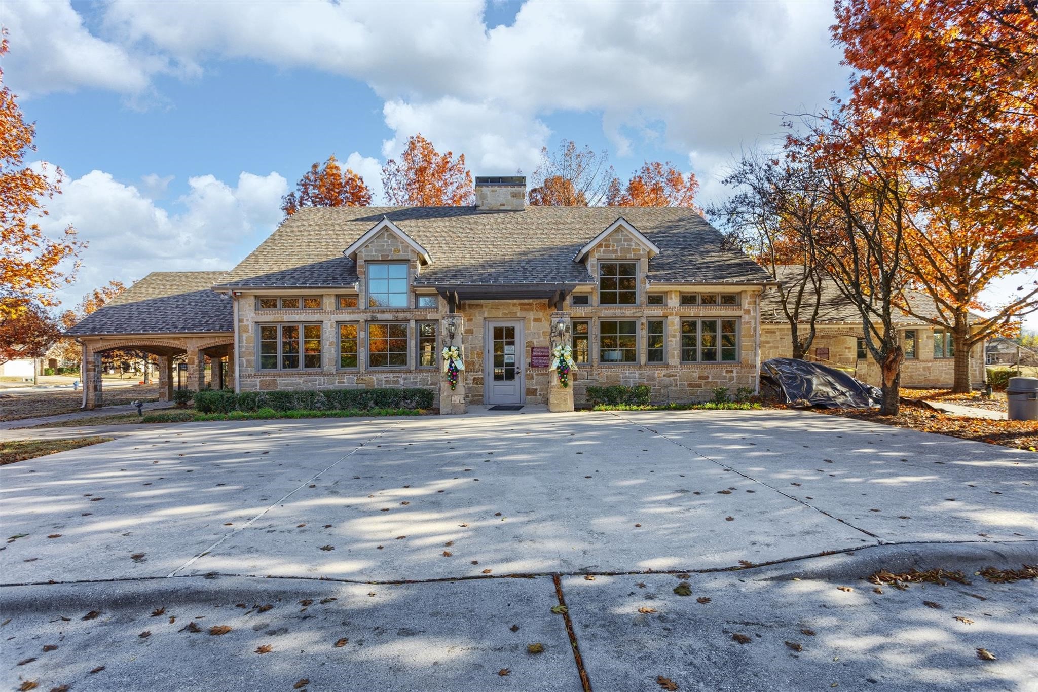 Stone-front building with a broad concrete driveway and orange autumn trees.