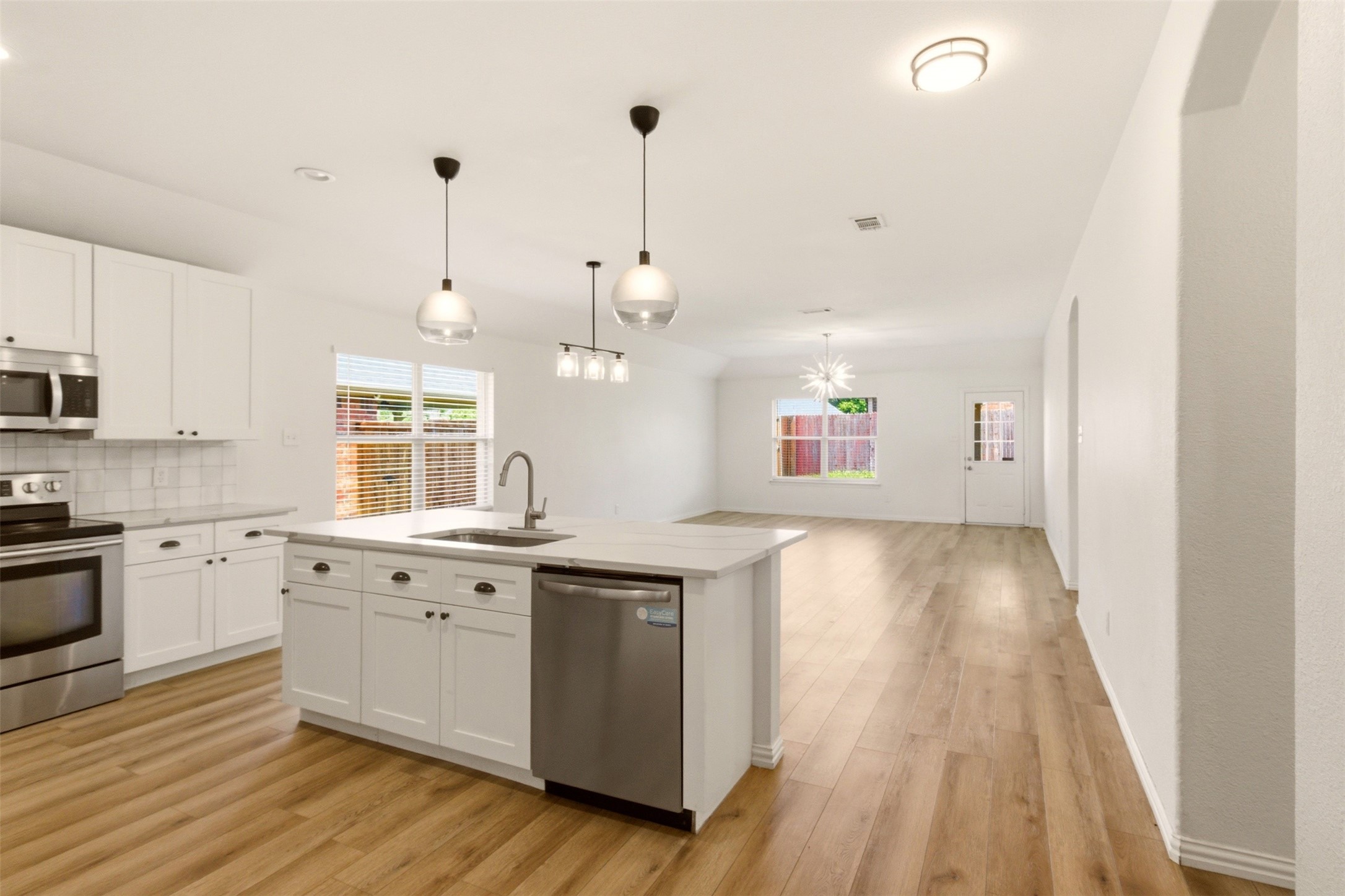 Vacant open-plan kitchen with a large island, white cabinets, stainless steel appliances, and wood-look flooring.
