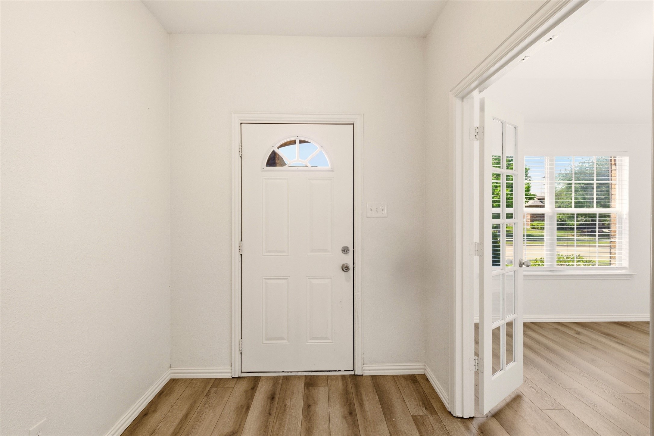 Entry foyer with a white front door, semicircular window, wood-look flooring, and open French doors.