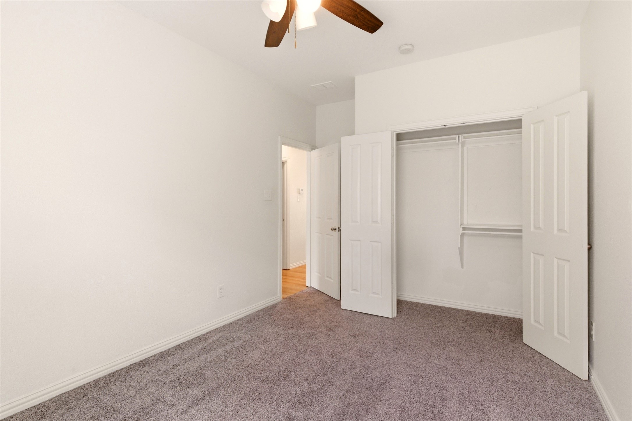 Empty bedroom with gray carpet, ceiling fan, and open double-door closet.