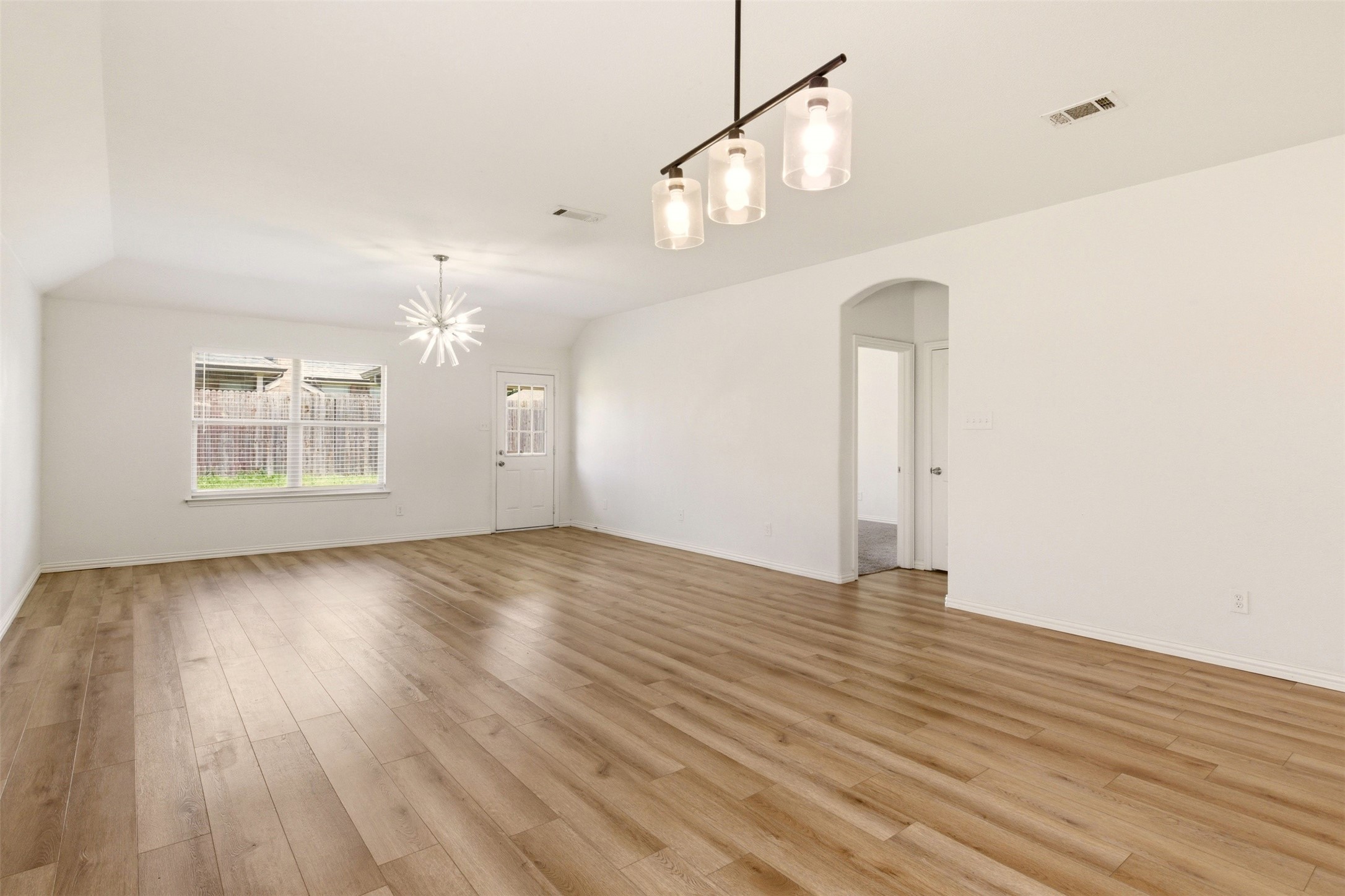 Empty living area with wood-look flooring, a window with blinds, and modern ceiling lights.