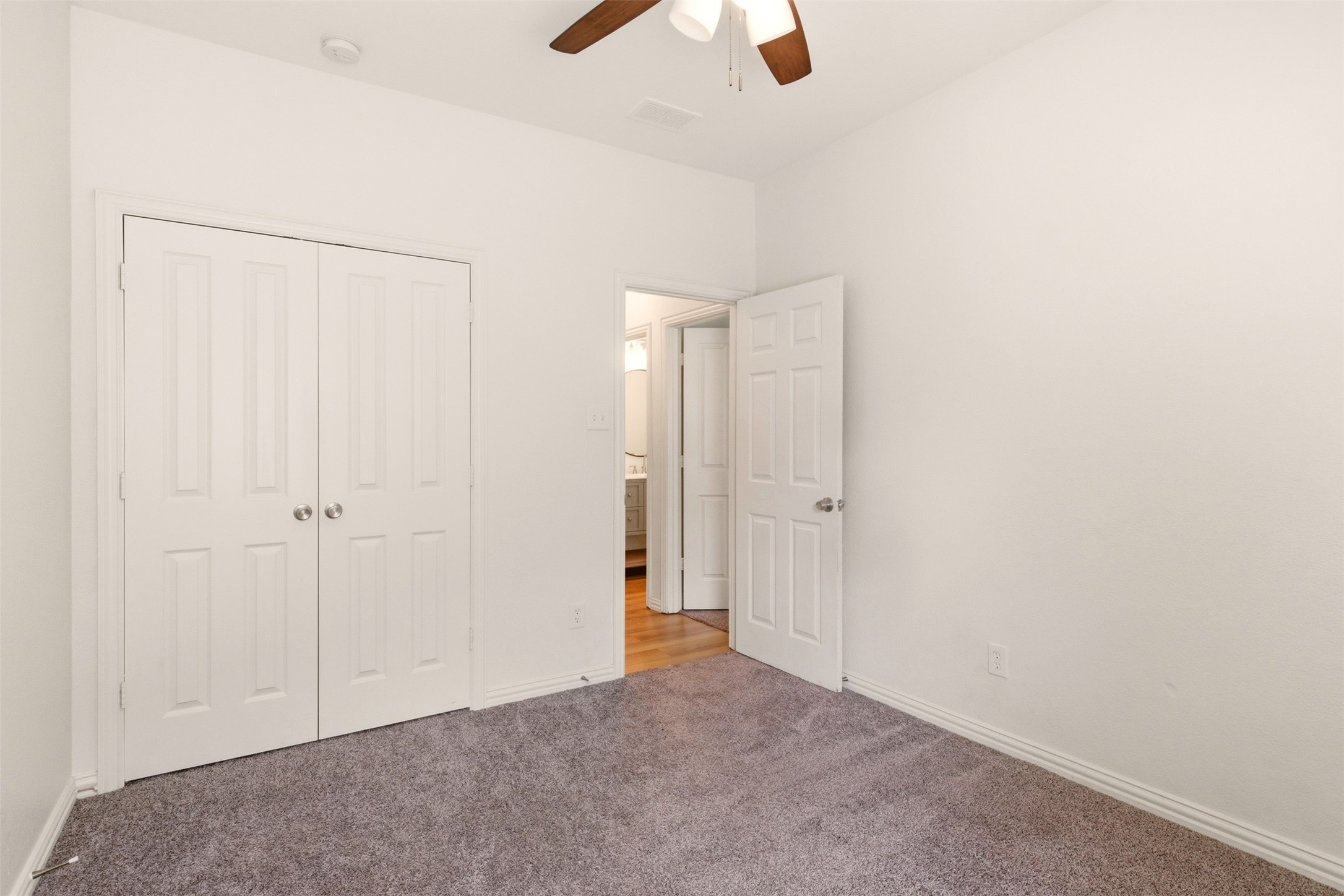 Empty carpeted bedroom with double-door closet and ceiling fan