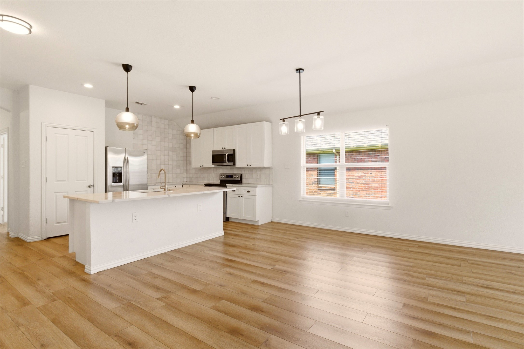 Open-plan kitchen with a large white island, stainless steel appliances, and light wood floors.