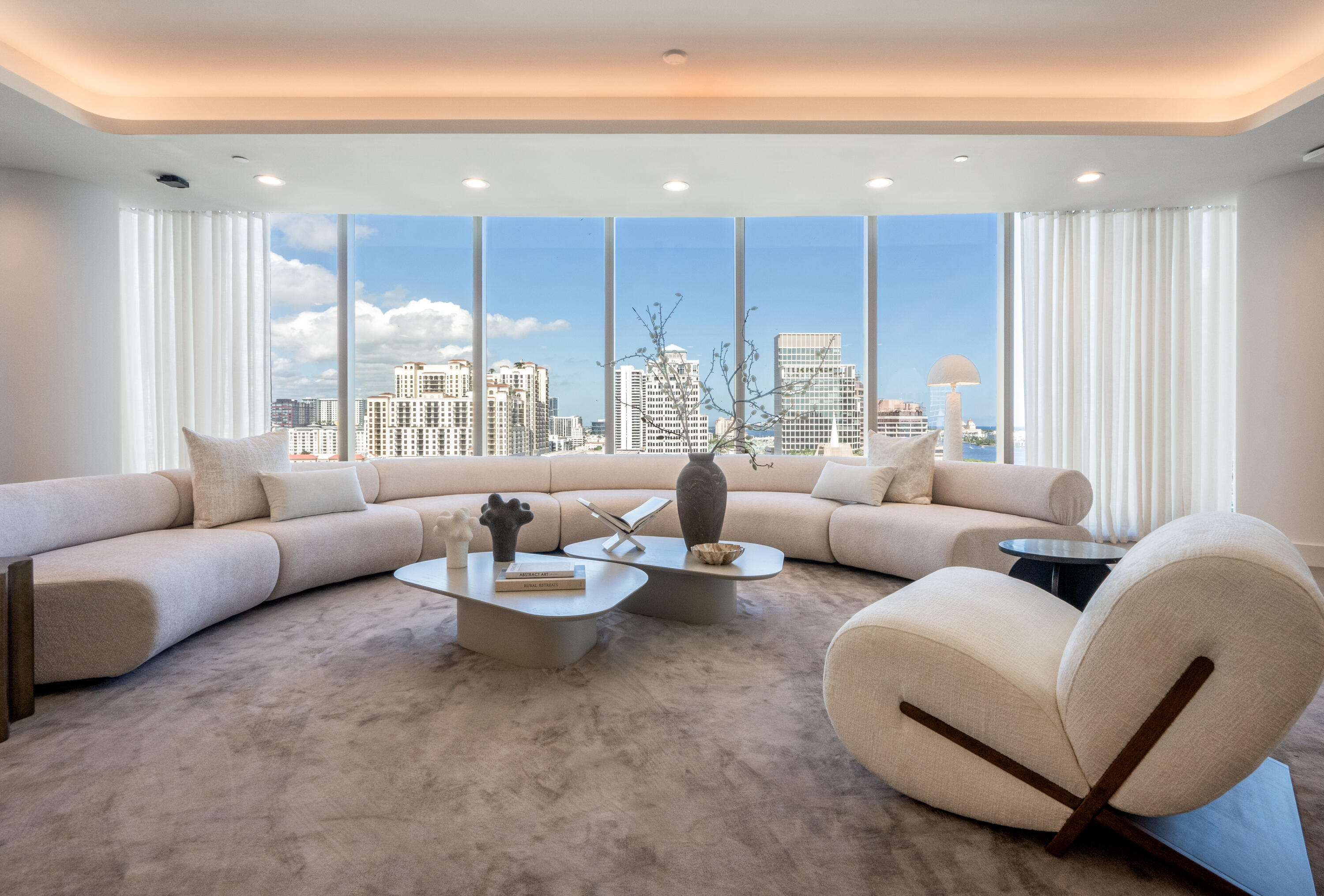 Living room with a curved cream sectional and panoramic city and water views.