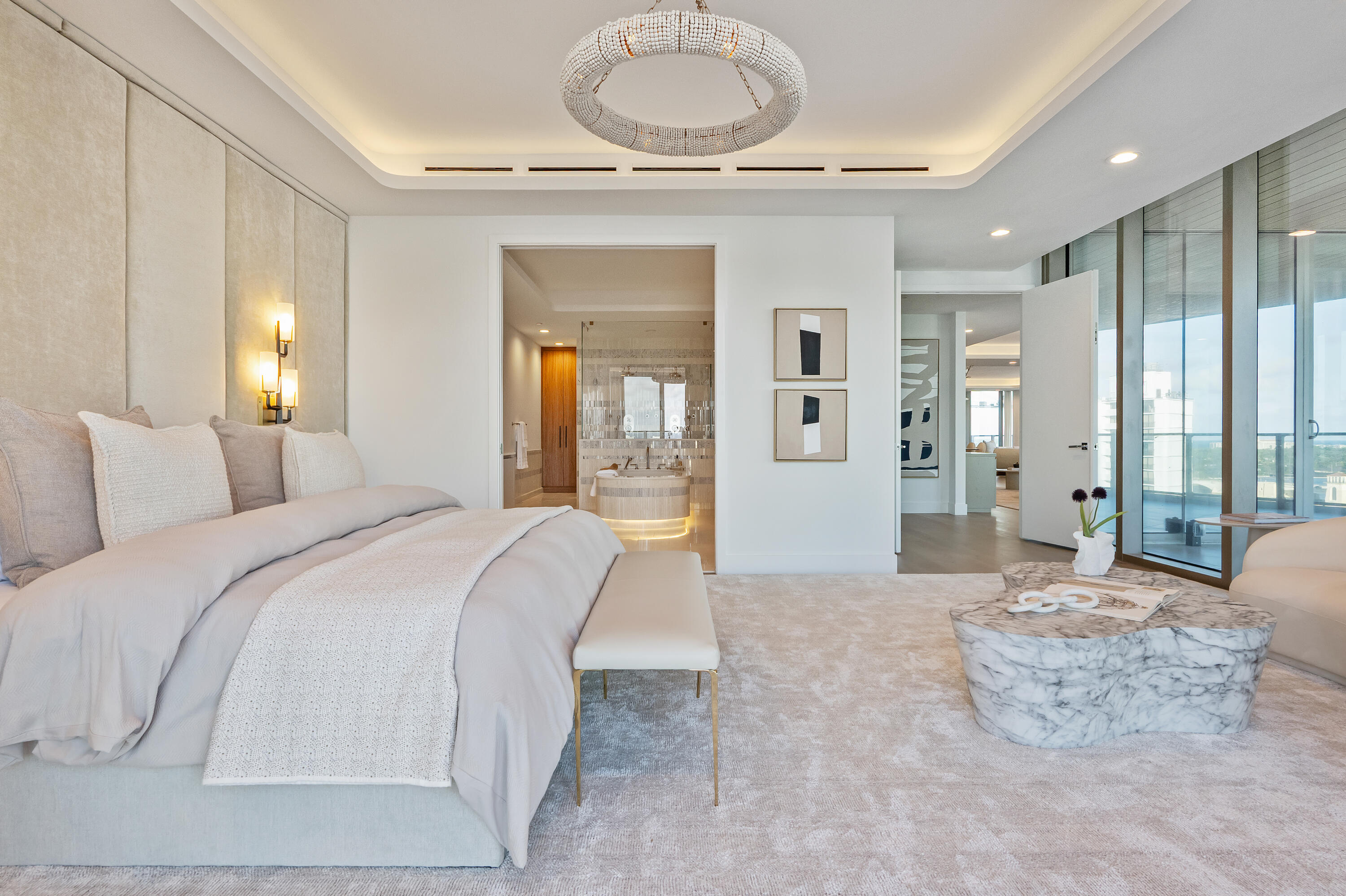Staged bedroom with an upholstered bed, crystal chandelier, and ensuite bathroom visible through the doorway.