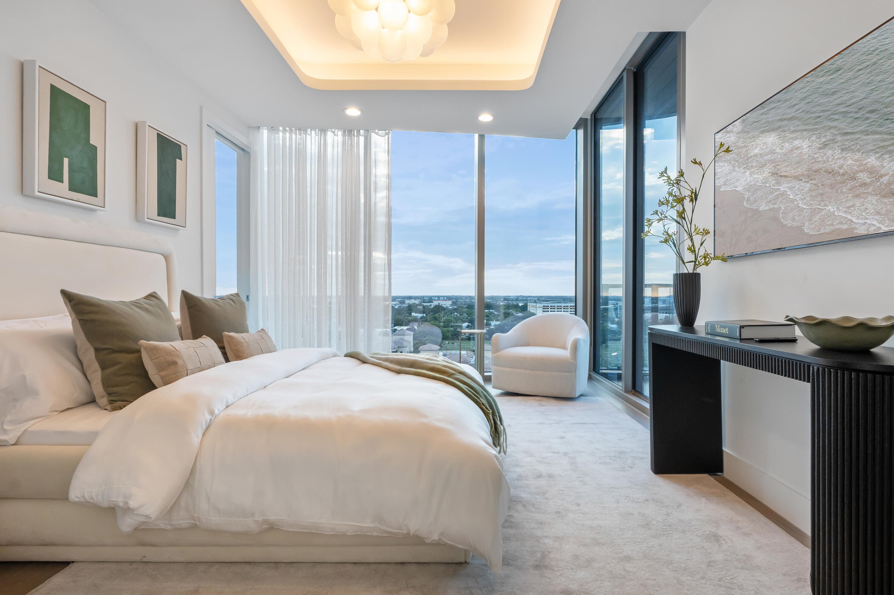 Contemporary bedroom with a white bed and floor-to-ceiling windows overlooking the city.