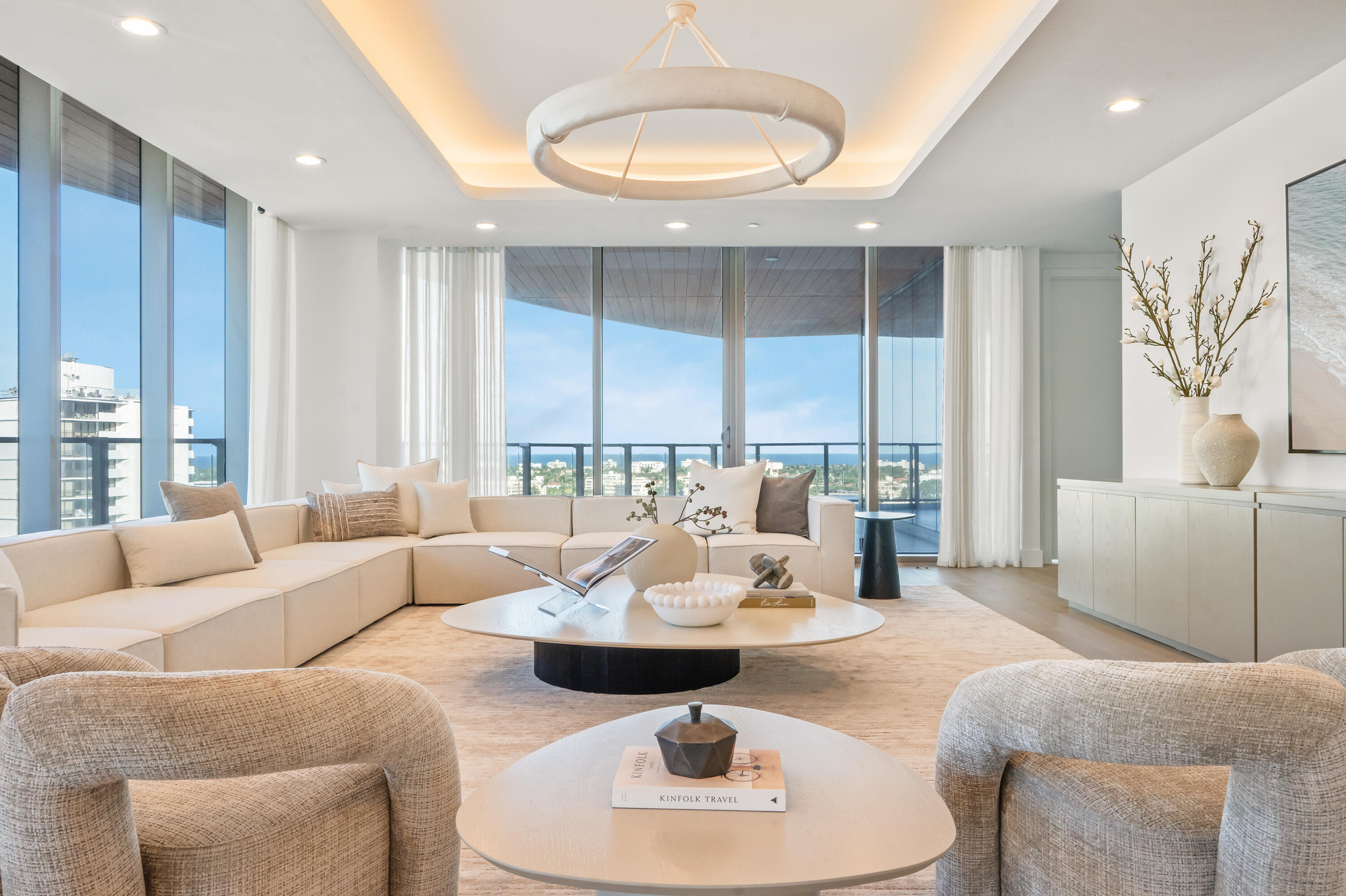 Furnished condo living room with a cream sectional and floor-to-ceiling windows overlooking the ocean and city.