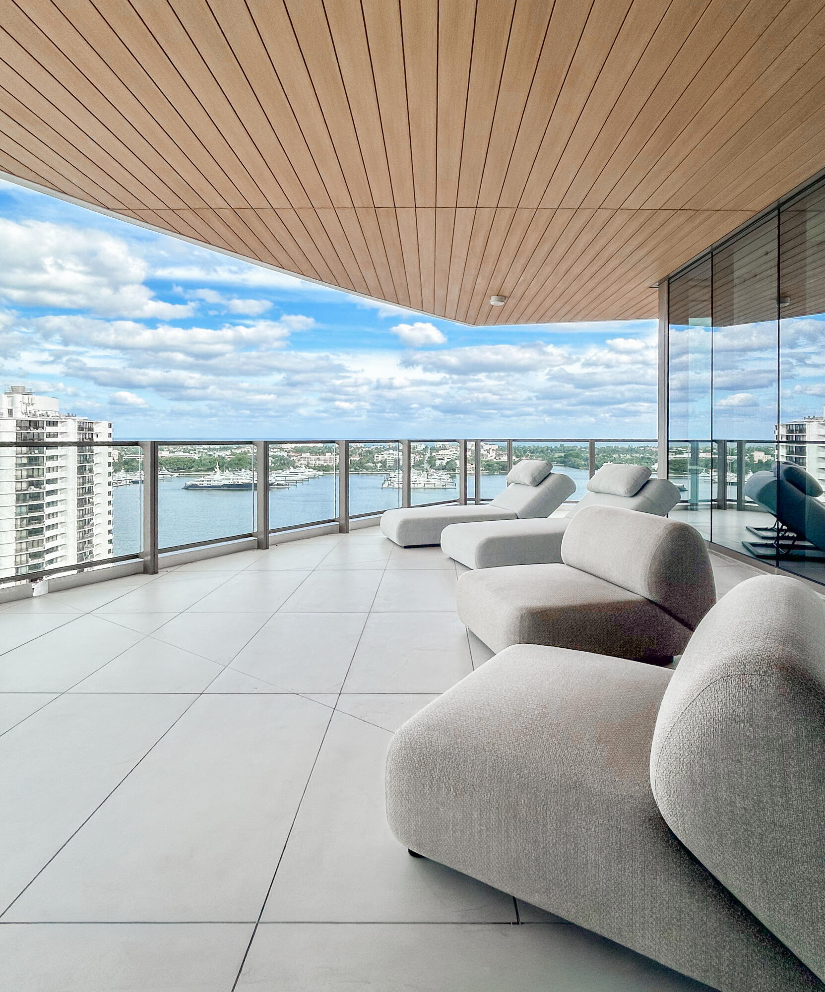 High-rise balcony with white lounge chairs overlooking a waterway and boats.