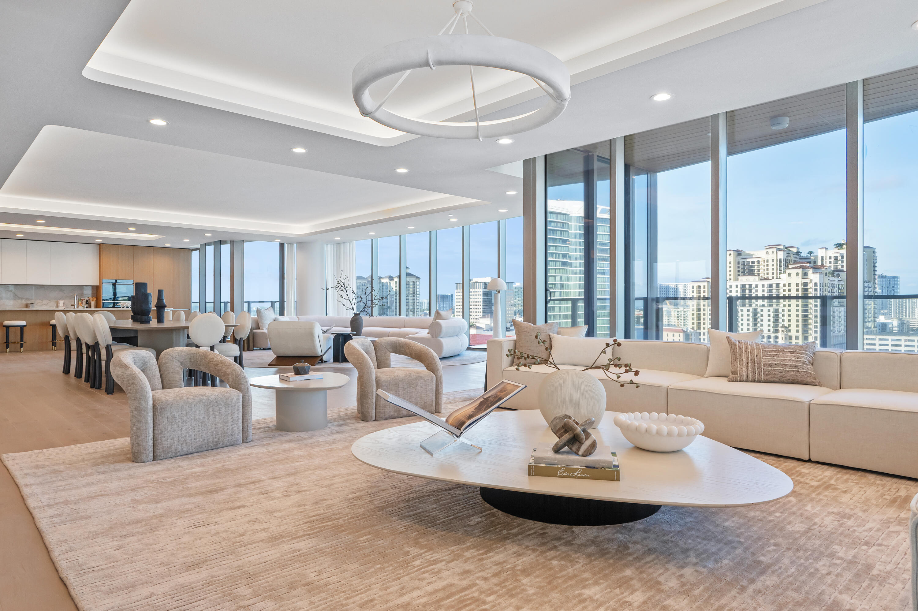 Staged condo great room with an open kitchen, sculptural chandelier, and city views through floor-to-ceiling windows.