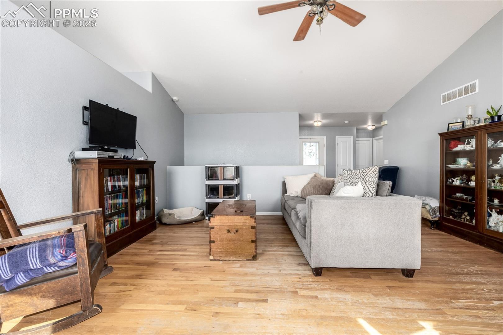 Living room with a gray sectional, wooden chest coffee table, television, and glass-front display cabinets.