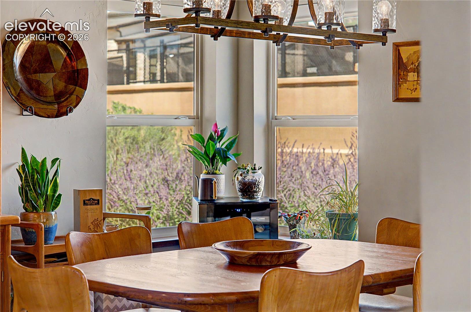 Dining room with a wooden table, rustic chandelier, and tall windows overlooking trees.
