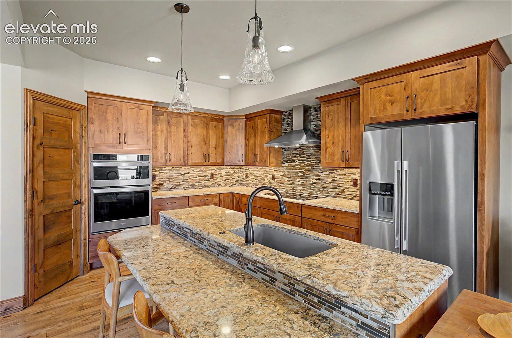 Kitchen with warm wood cabinets, granite island, stainless steel appliances, and a multicolored tile backsplash.