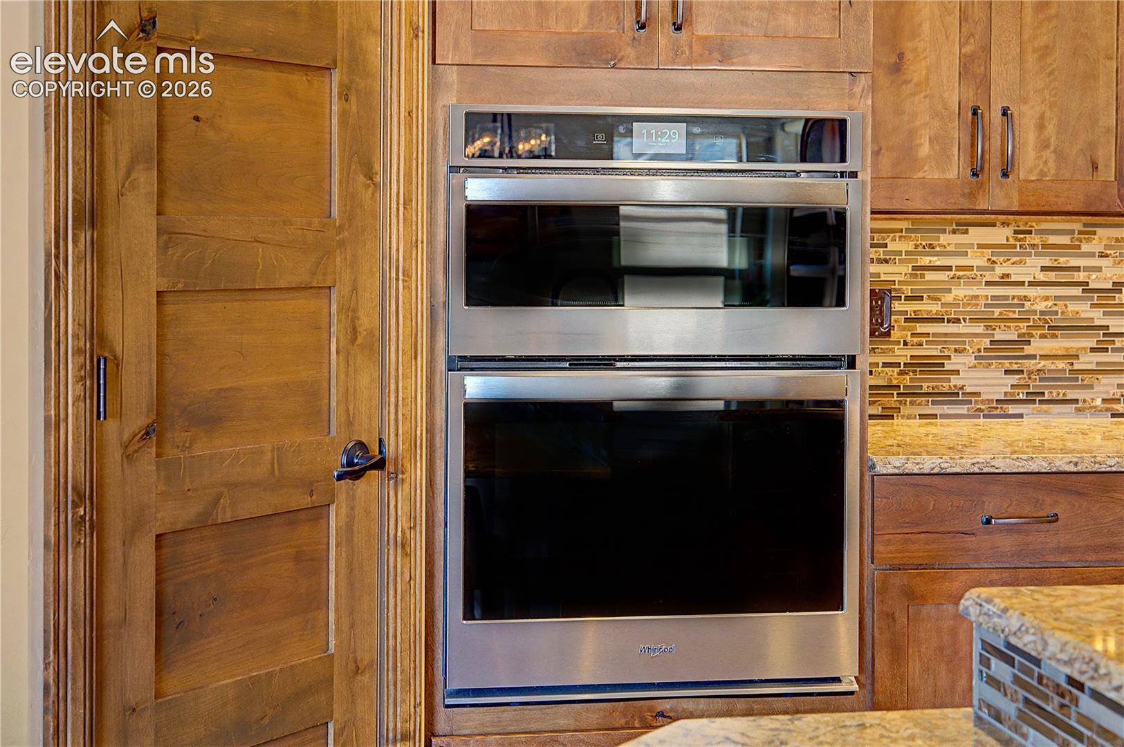 Kitchen with a stainless steel double oven, warm wood cabinetry, and mosaic tile backsplash.