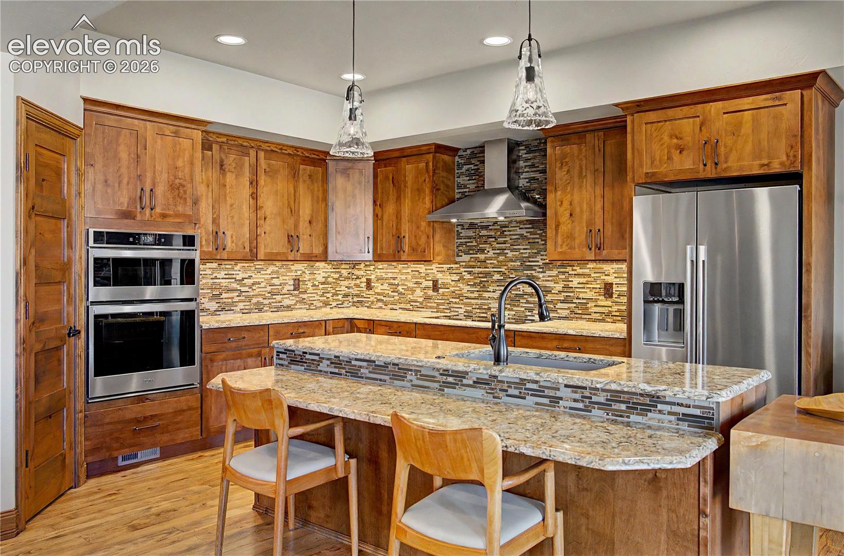 Kitchen with warm wood cabinets, a granite island, mosaic tile backsplash, and stainless steel appliances.