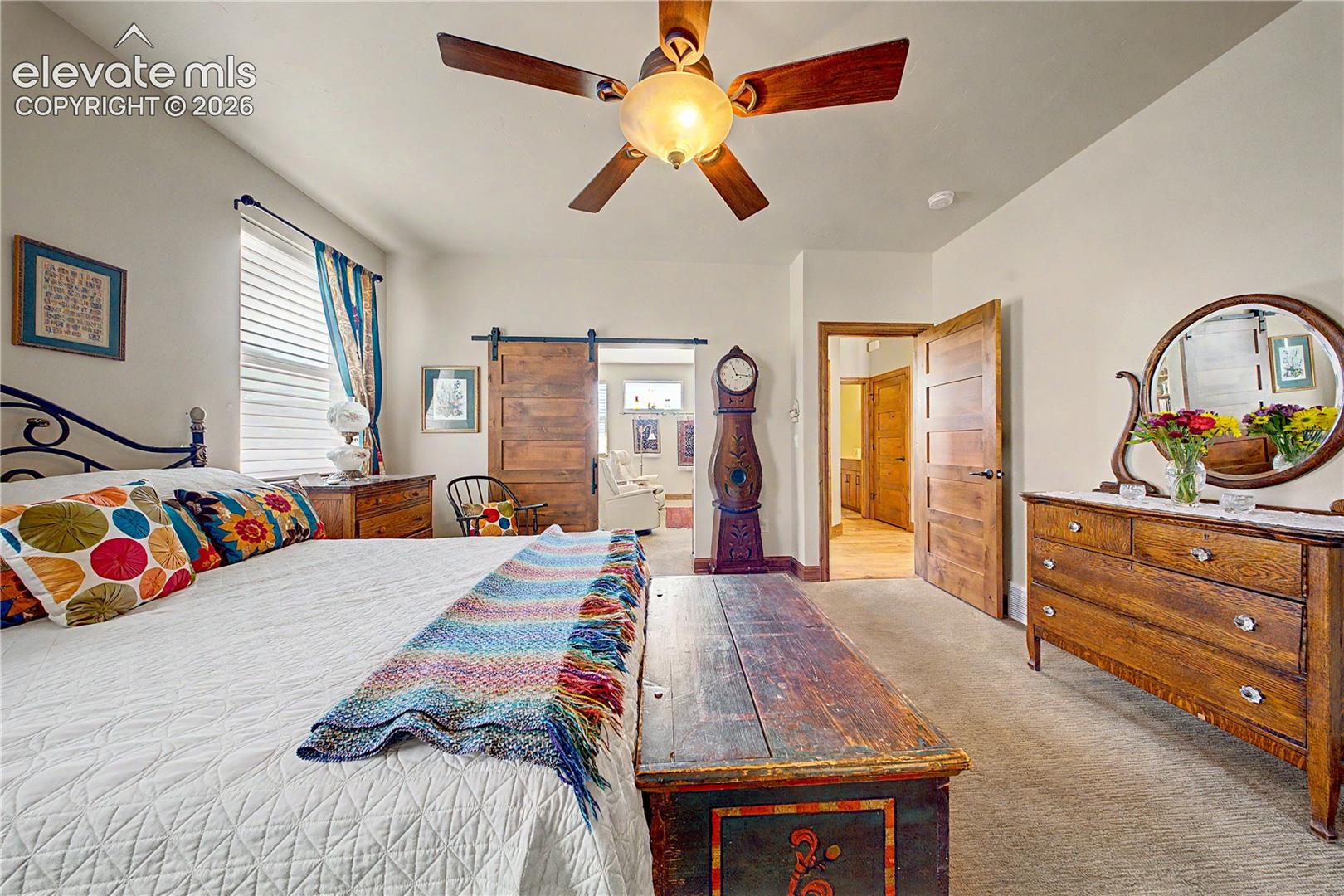 Furnished bedroom with a rustic barn door, ornate grandfather clock, and colorful bedding.