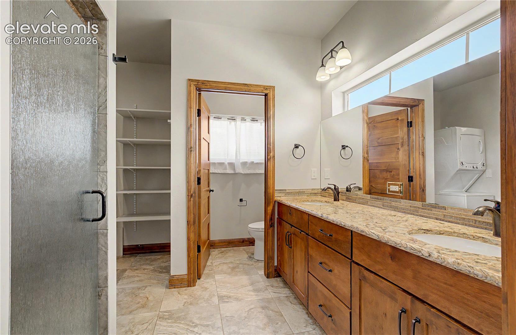 Bathroom with a long wood double vanity, stone counters, and a glass shower.