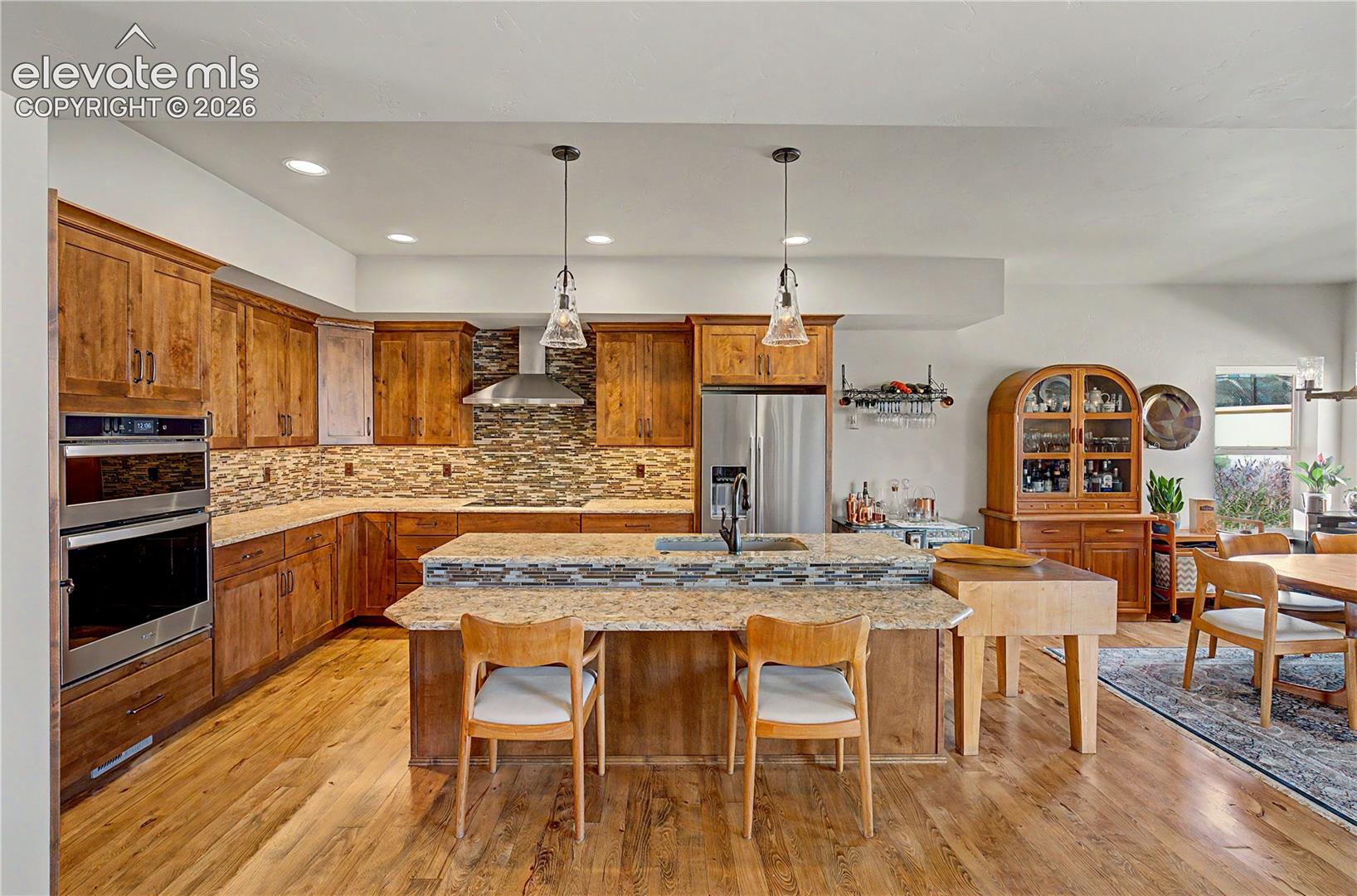 Kitchen with warm wood cabinets, stainless steel appliances, mosaic backsplash, and a large stone island.