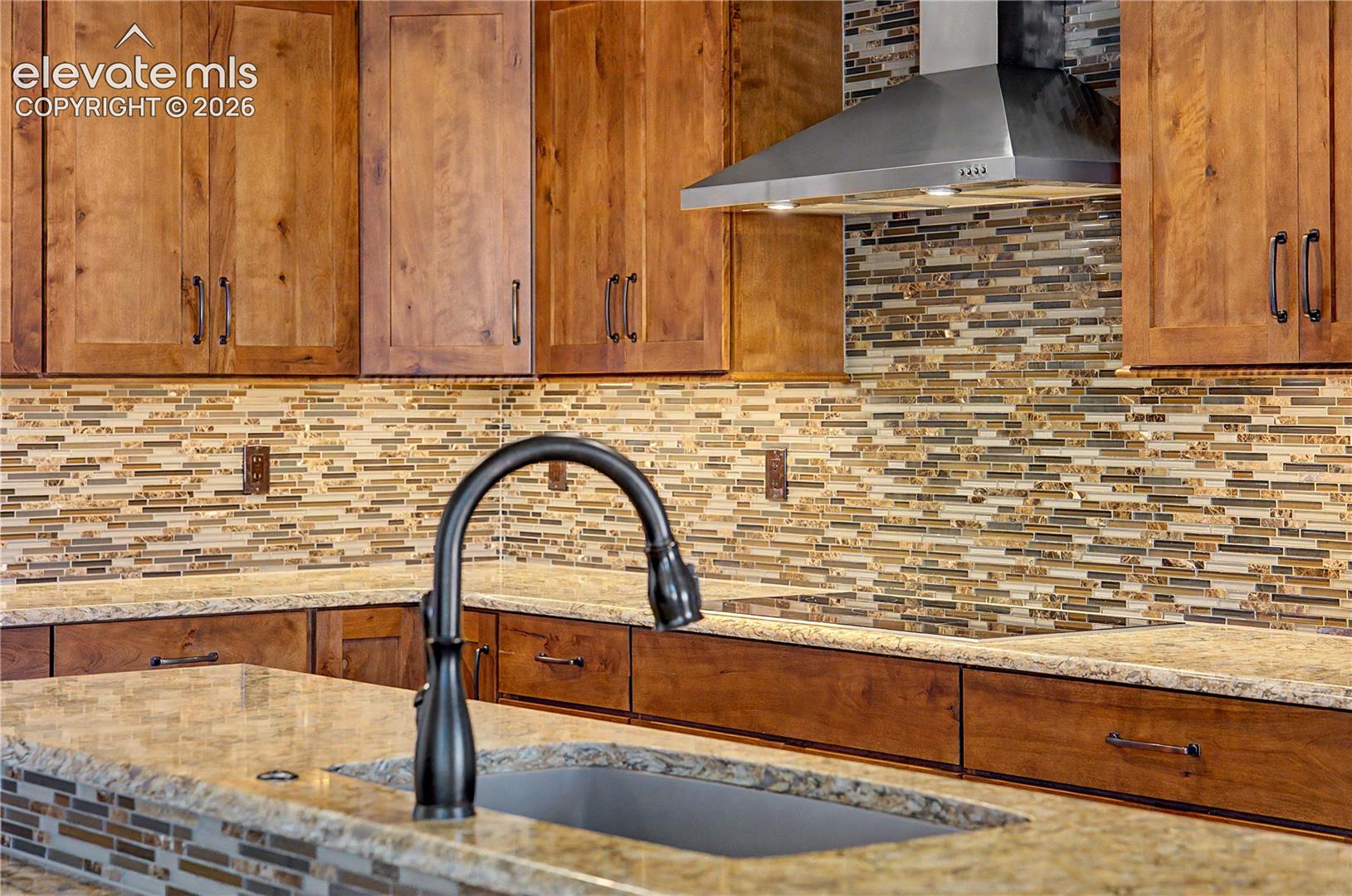 Kitchen with warm wood cabinets, mosaic tile backsplash, granite counters, and a large sink with an arched faucet.