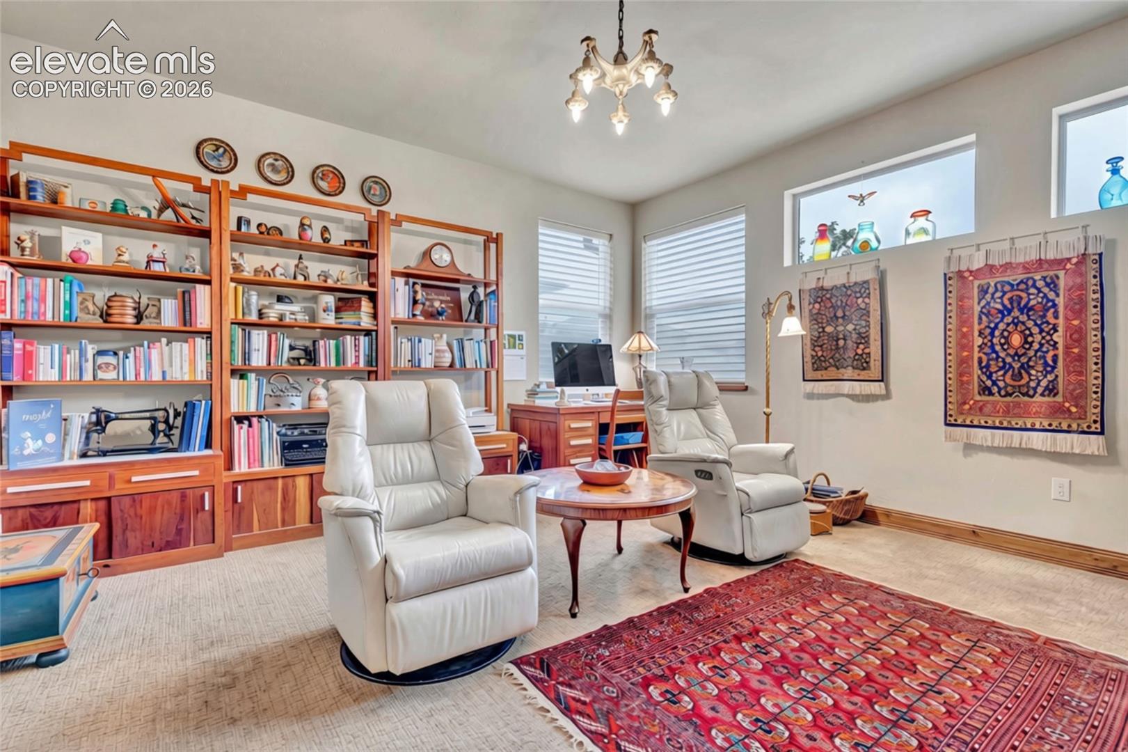 Furnished study with wooden bookshelves, white leather recliners, and colorful patterned rugs.